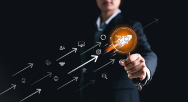 İş kadını, dijital oklarla başlangıç roket ikonunu işaret ederek, yenilik, büyüme, teknoloji, girişimcilik, başarı, liderlik ve gelecekteki iş gelişimini sembolize ediyor.