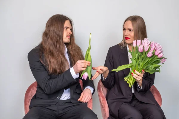 Man with long, brown hair presenting a single tulip to a beautif