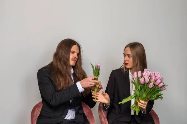 Man with long, brown hair presenting a single tulip to a beautif