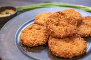 Koyu gri bir tabakta taze pişmiş tavuk nugget, yan yana soğanlar ve kremalı sos gri bir kâse içinde yuvarlak bir bez üzerinde ahşap bir masa üzerinde koyu bir peçete.
