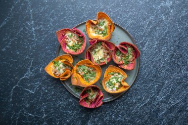 Taze, çıtır çıtır, renkli, yeşil ve peynirli tuzlu sepetler. Limon dilimleri ve gri tabakta maydanozla süslenmiş. Güzel, desenli, mavi granit bir yüzeye yerleştirilmiş. Yemek reklamı.