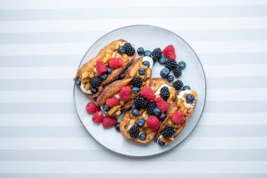 Krem peynirli taze yaban mersinli, çilekli, ahudutlu ve üzümlü taze ekmekler beyaz-gri şeritli bir yüzey üzerinde üzümlü ve üzümlü. Kopyalama alanı, metin için yer.