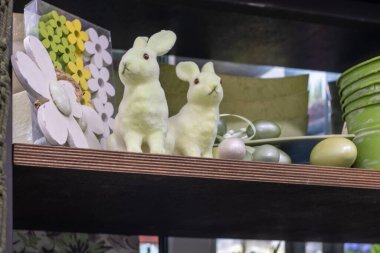 Kremalı Paskalya tavşanları, inci Paskalya yumurtaları, büyük beyaz ahşap bir çiçek ve renkli küçük ahşap çiçekler ve raflarda pastel yeşili kovalar. Kopyalama alanı