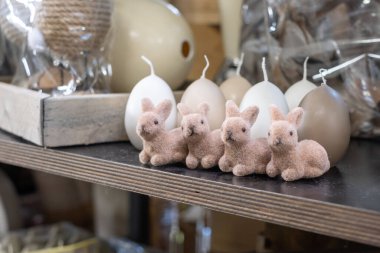 Şirin, eğlenceli, tüylü, pembe Paskalya tavşanları ve açık renkli büyük mumlar. Karanlık bir raftaki Paskalya yumurtaları gibi. Arka plandaki bir kutuda paketlenmiş dekorasyon malzemeleri. Kopyalama alanı