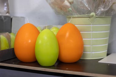 Güzel, parlak, turuncu ve sarı mumlar karanlık bir raftaki Paskalya yumurtaları gibi. Süslemeleri ve parlak sarı mumları olan sarı renkli bir kova..