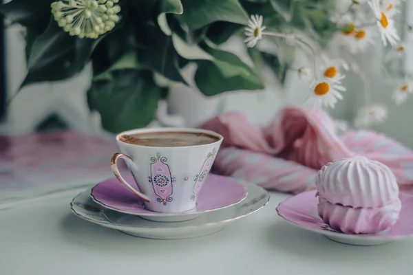 白いテーブルの上のソーサーで豪華な壊れやすい白いピンクのコーヒーカップとパフィーのようなピンクのマシュマロ スタイリッシュなピンクのドットスカーフ 背景に白い花瓶の美しい晴れた日 — ストック写真