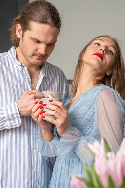 A mysterious man and a beautiful confident woman with red lips and nails. A couple in light blue clothes drinking coffee and getting to know each other\'s character. Copyspace