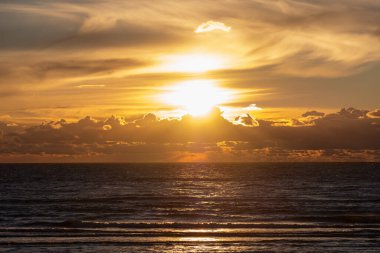 Denizde resim gibi gün batımı. Denizde güneş ışığının yansıması, ufukta bir sıradağ gibi bulutlar ve arka planda bulutların üstündeki güneş. Uzayı kopyala Alıntılar için arkaplan.