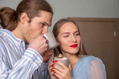 Açık mavi elbiseli güzel uzun saçlı iki genç kahve içiyor. Bir erkek düşünceli ve bir kadın kameraya gülümseyerek bakıyor. Kapı arka planda. Kopyalama alanı