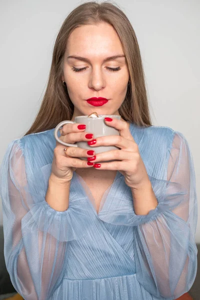 stock image Beautiful young serious woman in light blue dress, with gorgeous long hair, red lips and nails, ring finger, looking at coffee with whipped cream cap.