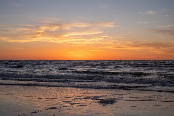 A peaceful, meditative, quiet moment - the sun is already over the horizon, white waves in the sea and orange-yellow clouds in the background. High quality photo