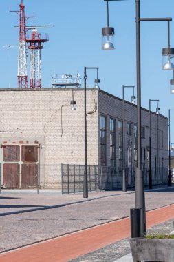 Kocaman pencereleri, kapıları ve metal çitleri olan sanayi binası. Elektrik direkleri ve arka planda açık mavi gökyüzü. Açık hava fenerleri ve renkli kaldırımlar ön planda. Uzayı kopyala Yüksek kalite fotoğraf