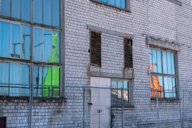 Paslı pencere çerçeveli tuğla bir bina, metal bir çitin yanında. Yeşil ve turuncu renkler pencerelere yansıyor - iyimserlik, doğallık, sağlık. Yüksek kalite fotoğraf