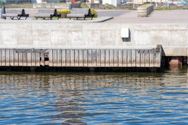 Deniz, beton döşeme ve ahşap tahtalarla güçlendirilmiş sahil. Arka planda, bir bank, bir çiçek yatağı ve açık vazolarda çiçekler. Uzayı kopyala Alıntılar için arka plan. Yüksek kalite fotoğraf