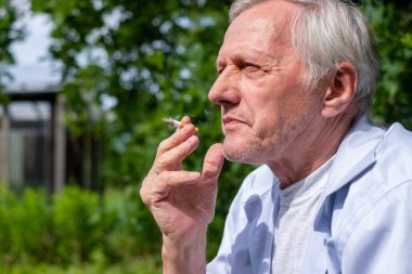 Parkta sigara içen yaşlı bir adam, yaşam tarzı ve yaşlanma, sağlıksız alışkanlıklar ve bağımlılıklar, sigorta reklamı hakkında konuşmak için uygun bir fotoğraf. Yüksek kalite fotoğraf