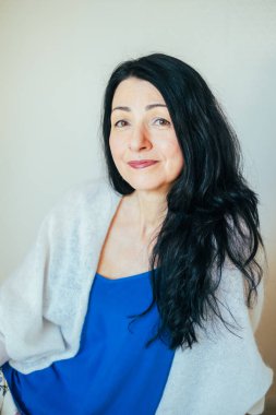Kendinden emin orta yaşlı bir kadın, ışıl ışıl gülümseyen, mavi elbiseli, menopoza girmiş. Kadınların orta yaş refahı ve duygusal açıdan zor zamanları için mükemmel. Yüksek kalite fotoğraf