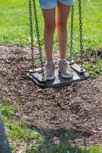 The focused view on a girls feet on a swing in a playground set evokes the essence of childhood play in a park setting, used for health insurance.. High quality photo