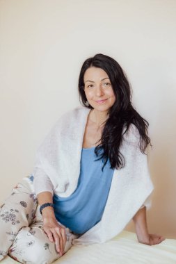 Siyah saçlı, mavi bluzlu, beyaz şallı, rahat oturan gülümseyen bir kadın. Onun rahat duruşu ve sıcak ifadesi evcimen bir memnuniyeti çağrıştırıyor. Yüksek kalite fotoğraf