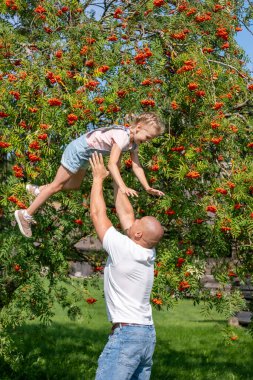 Coşkulu bir kız, havanın ortasında babasını, yemyeşil bir bahçe, aile bağları ve doğanın oyun bahçesi, hayat ve sağlık sigortası ile çevrili halde yakalar. Yüksek kalite fotoğraf