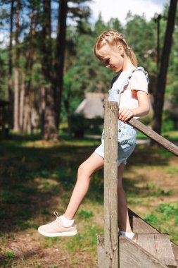 Yeşil doğa manzaralı meraklı bir kız yere bakıyor. Bu, doğadaki macera oyunlarının ve keşiflerin özünü yakalar. Yüksek kalite fotoğraf