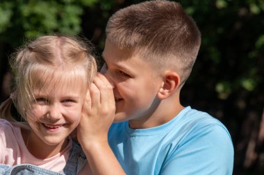 Kardeş sırları çimenli bir arazide gözler önüne serilirken, bir çocuk Ulusal Kardeşler Günü için kullanılan sırıtan kız kardeşiyle bir fısıltı paylaşmak için eğildi, doğada mutluluk ve kaçışçılık. Yüksek kalite fotoğraf