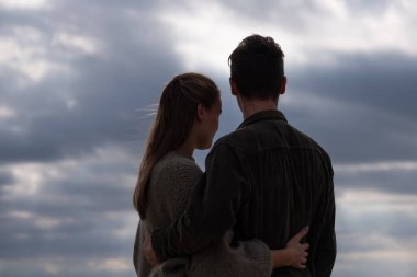 Yakın bir kucaklaşmadaki bir çiftin, denizin üzerindeki dramatik bulutlu gökyüzüne bakışları, düşünmeyi ve birlikteliği sembolize ediyor, birbirine aşık iki kişi için doğada bir randevu. Yüksek kalite fotoğraf