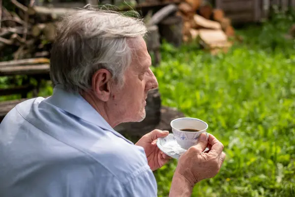 Man in profile holding a teacup, gazing into the distance in a lush garden a moment of quiet reflection, and elderly peace. High quality photo