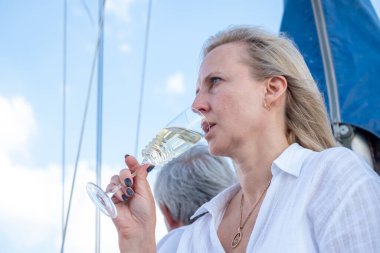 Sakin bir yat sahnesi, bir bardak şaraptan hoşlanan sarışın bir kadın, okyanusa bakan bir adam, rahatlama ve refahın simgesi. Yüksek kalite fotoğraf