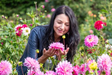 Orta yaş kadını çiçek bahçesinde canlılık ve neşe hisseder olgunluğun, bilgeliğin ve sonbahar konseptinin özünü yakalar.