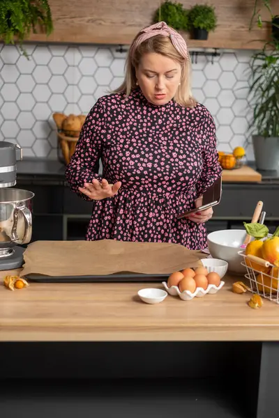 Şık bir mutfakta, fırıncı kadın şaşırmış görünüyor. Tezgahta yumurta ve portakallı malzemeler hazırlıyor. Hazırlık konsepti.