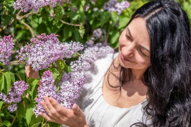 Güneşli bir günde elinde leylak çiçekleri tutan gülümseyen kadın, doğanın güzelliğinin tadını çıkarıyor, elinde mor çiçeklerle portre, doğa bağlantısı konsepti