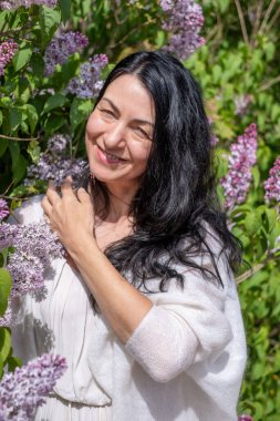 Gülümseyen kadın canlı leylak çiçeklerinden hoşlanır, çiçek açan bir bahçe atmosferiyle çevrili, doğa kavramı