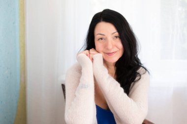 Samimi bir ortamda gülümseyen zarif bir kadın, günlük kıyafet, doğal ışık, neşeli ruh hali, sabah atmosferi, kapalı mekan portresi, rahat yaşam tarzı anı, sakin konsept