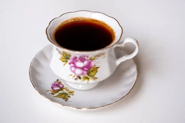 Çok güzel işlenmiş bir porselen fincan zengin, koyu bir kahve tutar. Rengarenk çiçek desenleriyle süslenmiş zarif bir fincan üzerinde dinlenir. Huzurlu bir sabah keyfi için idealdir..