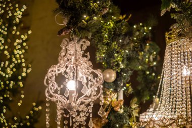 Entrika ile tasarlanmış avizeler kristal aksanlar ve sıcak ışıklarla parıldıyor, yeşillik ve tatil dekorasyonlarıyla süslenmiş şenlikli bir atmosfer yaratıyorlar..