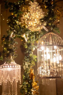 A beautiful display of shimmering chandeliers and a decorative birdcage, all surrounded by lush garlands and twinkling lights, creating a warm atmosphere. clipart