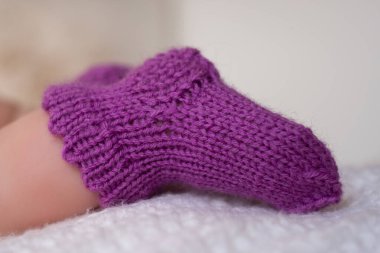 A pair of cozy purple knitted booties for infants is placed delicately on a soft white blanket, showcasing their adorable texture and warmth. clipart