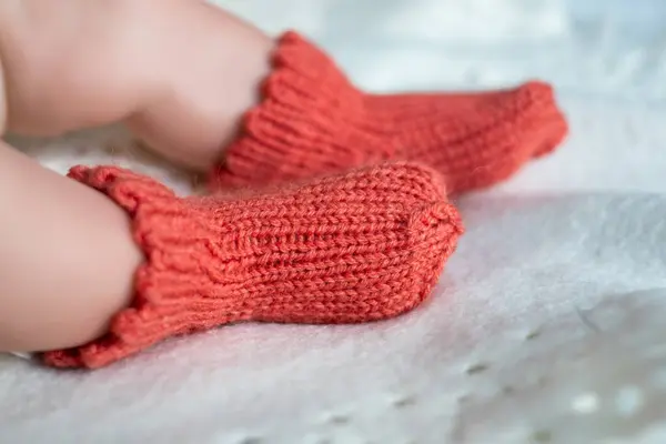 Küçük ayaklar, yumuşak beyaz bir battaniyenin üzerinde uzanan parlak turuncu örülmüş paçalara rahatça yerleşir. Nazik ayar sıcaklığı ve özeni vurgular..