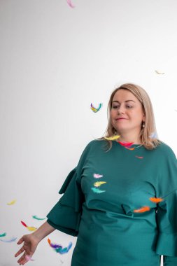 Yeşil elbiseli, sarı saçlı bir kadın, parlak, minimalist bir iç mekan ortamında kıvrılarak neşeli ve kaprisli bir anı yakalayan canlı kağıt kuşlar gibi sakince duruyor..