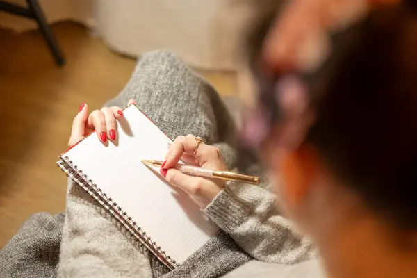 Sıcak, davetkar bir yerde oturan bir insan, elinde altın bir kalemle yaratıcılığını ve yansımasını boş bir deftere yazmaya odaklanır..