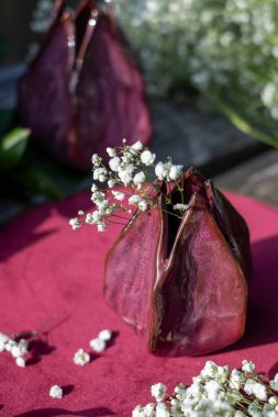 A handmade vase holds a charming arrangement of white flowers, placed on rich red fabric, creating a warm, inviting atmosphere that highlights nature's beauty. clipart