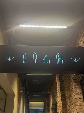 Aydınlatılmış tuvalet tabelasında erkek, kadın, erişilebilir ve aile tesisleri için simgeler gösterilerek, çağdaş bir iç mekan ortamında net yönler gösterilmektedir.