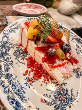 Meyve ve kırmızı sosla kaplı kremalı bir tatlı. Dekoratif bir tabakta güzelce sunuluyor. Aşçılık sunumunun sanatını vurguluyor.