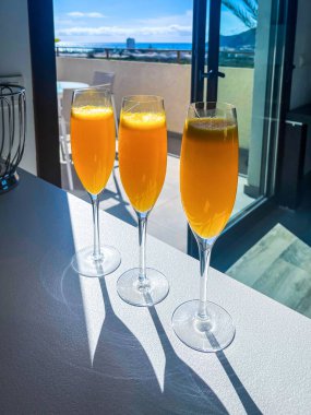 İçi ferahlatıcı turuncu mimoza kokteylleriyle dolu üç şık şampanya kadehi parlak bir tezgahta sergileniyor, neşeli ve davetkar bir brunch sahnesi yaratıyor.