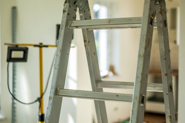 Metal merdiven, aletler ve malzemelerle çevrili iyi ışıklandırılmış bir odada duruyor. Ev yenileme ve inşaat işlerinde bir ortam yaratıyor.