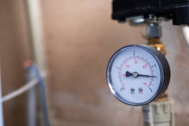 Basınç göstergesi, aletler ve ekipmanlarla çevrili mekanik bir ortamda ölçümü gösteren, endüstriyel işlevselliği vurgulayan bir boruda belirgin bir şekilde gösteriliyor