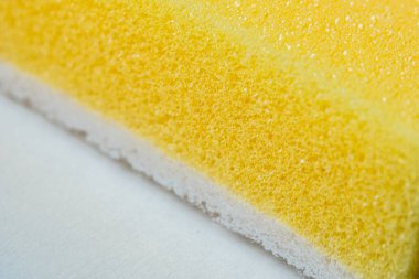 Bu yakın plan resim, gözenekli yapısını ve yumuşak yüzeyini vurgulayan, çeşitli kullanımlar için ideal, detaylı doku ve desenlere sahip sarı bir sünger içerir.