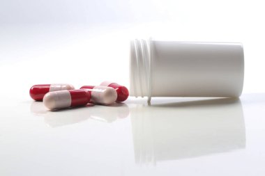 Beyaz arka planda beyaz şişe ve kırmızı antibiyotik kapsüller