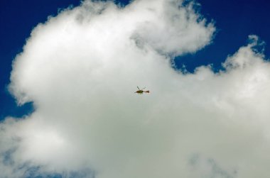Güneşli bir günde beyaz kabarık bulutlar ve mavi gökyüzü ile Londra Hava Ambulansı 'nın yerden görünüşü. Helikopter acilen acil tıbbi yardıma ihtiyacı olan insanları uygun hastanelere götürüyor..