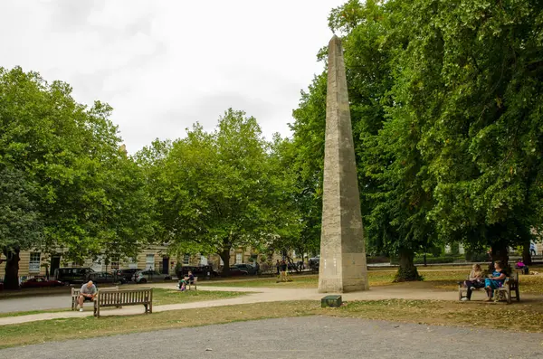 stock image September 3, 2022: people resting on the benches surrounding the historic obelisk in Queen's Square in the centre of the city of Bath, Somerset on a late summer afternoon.